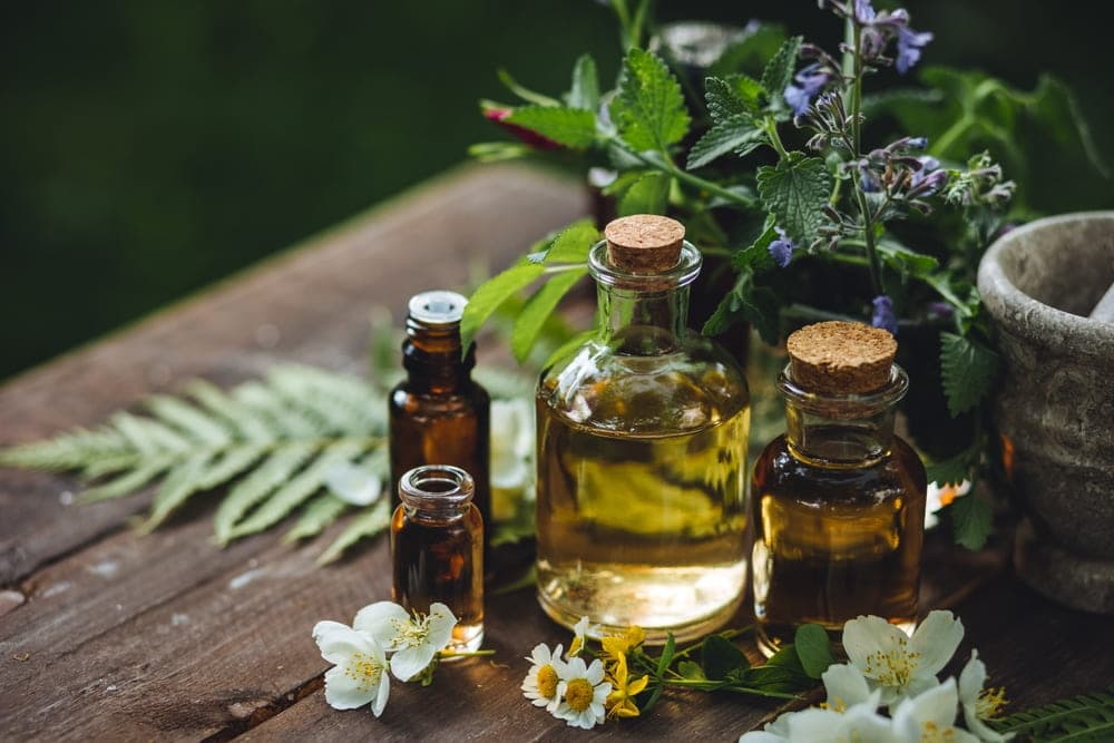 Soothing herbal essential oils in glass bottles with fresh flowers, representing natural spa treatments at Makkha Spa in Chiang Mai.
