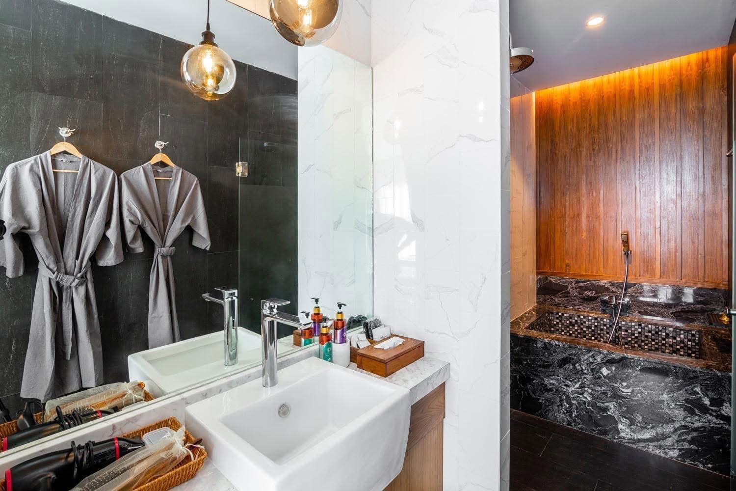 Luxurious spa bathroom with elegant black and white marble accents, modern sink, toiletries, and a relaxing wooden-walled shower area with black marble flooring at Makkha Spa Chiang mai.