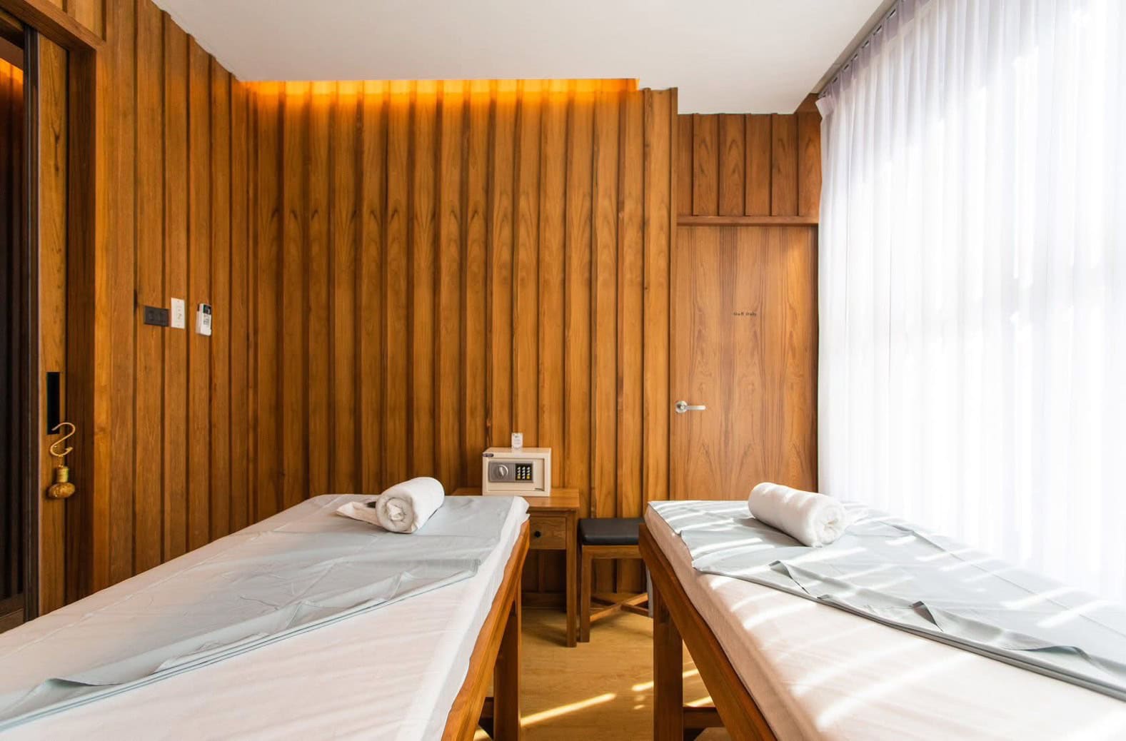 Clean, cozy massage room with two treatment beds, wooden interior walls, and soft white curtains providing natural light at Makkha Spa in Chiang Mai.