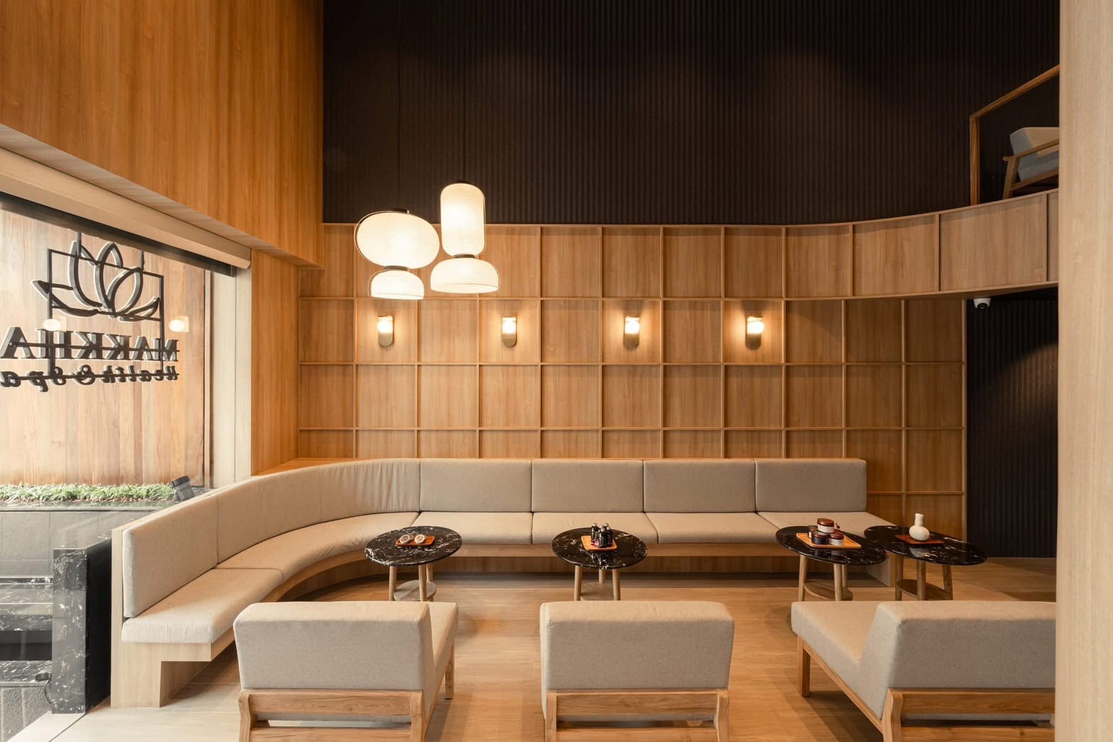 Luxurious spa waiting lounge with beige seating, wooden wall panels, modern pendant lights, and a welcoming atmosphere at Makkha Health & Spa in Chiang Mai.