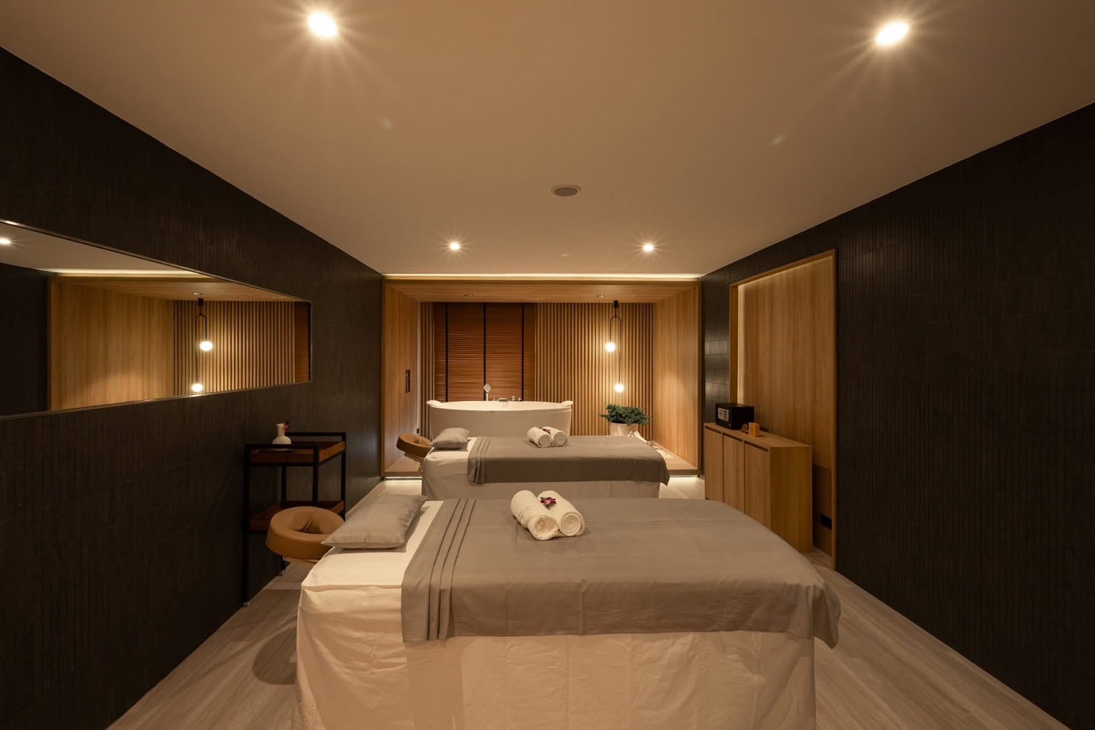 Luxurious massage room at Makkha Health & Spa Chiang Mai featuring two massage tables, soft lighting, and modern wooden decor for a relaxing spa experience.