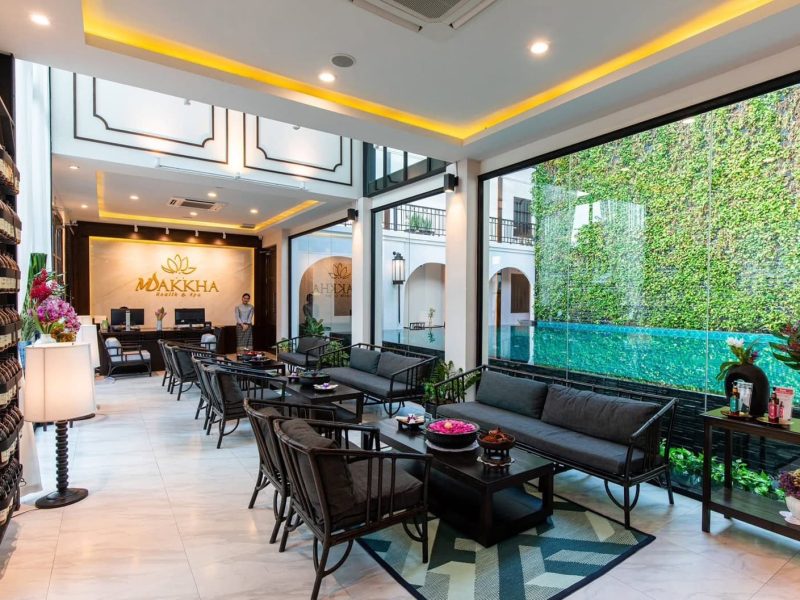 Elegant spa reception area at Makkha Health & Spa in Chiang Mai with modern decor, indoor seating, and lush outdoor pool view, offering a tranquil and luxurious wellness experience.