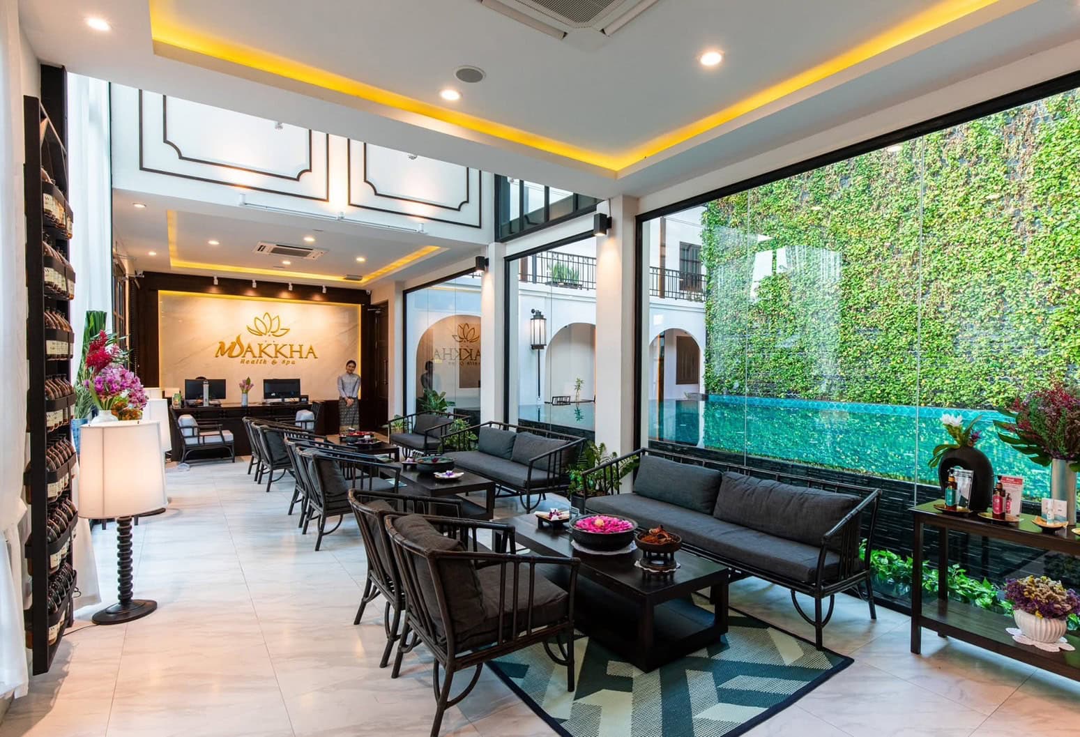 Elegant spa reception area at Makkha Health & Spa in Chiang Mai with modern decor, indoor seating, and lush outdoor pool view, offering a tranquil and luxurious wellness experience.