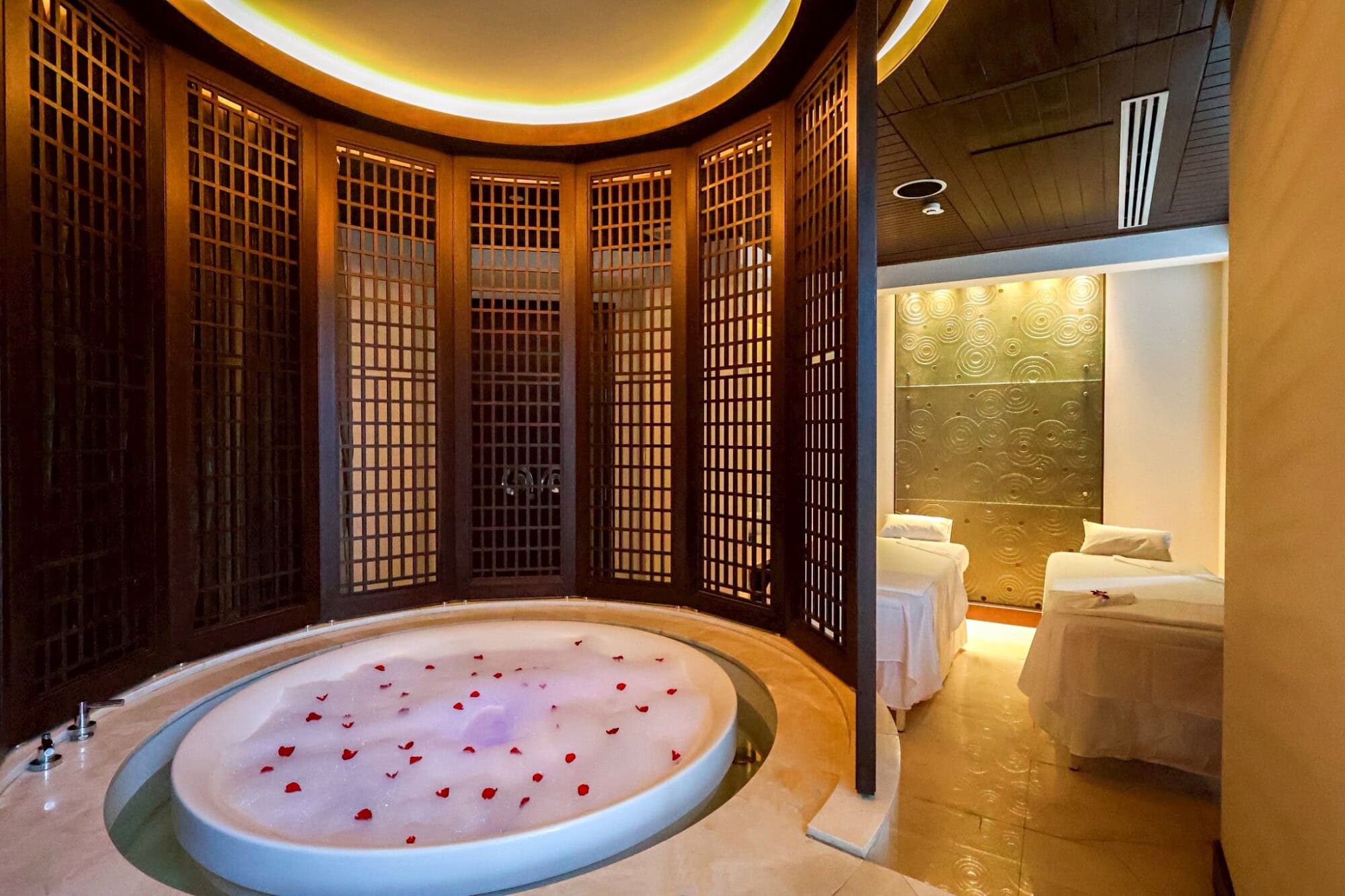 Luxurious spa treatment room with a large bubble bath decorated with rose petals, private beds, and elegant Asian-inspired wooden decor at Makkha Spa in Chiang Mai, offering the best spa experience.